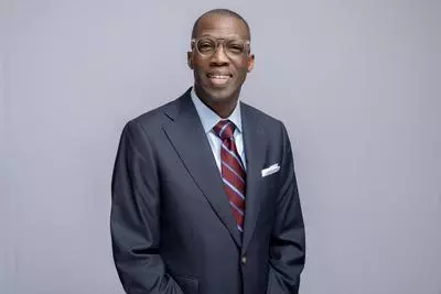 Commissioner Arnold standing in front of a gray background with navy blue suite and striped tie.